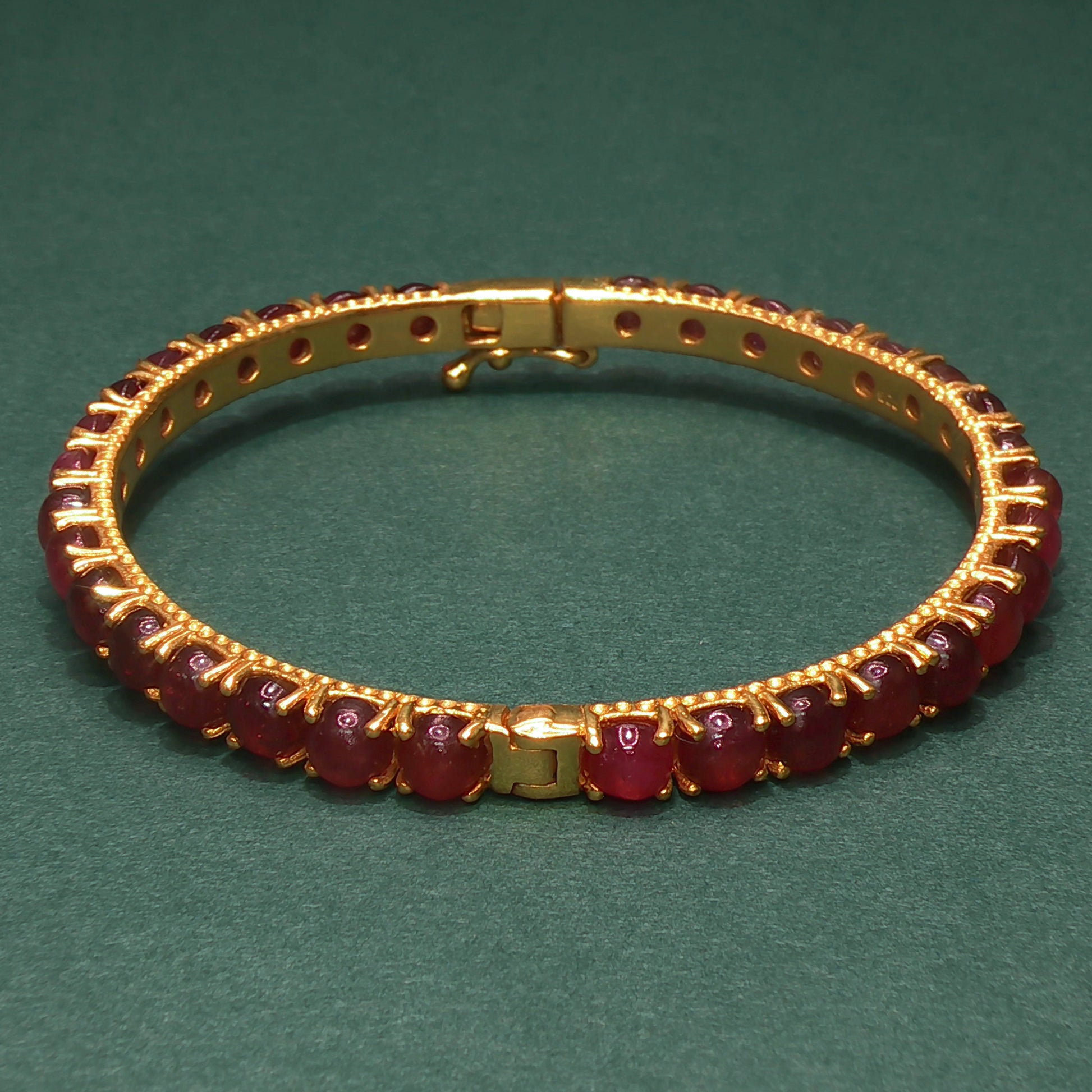 Gold bracelet with gemstones on a green background


