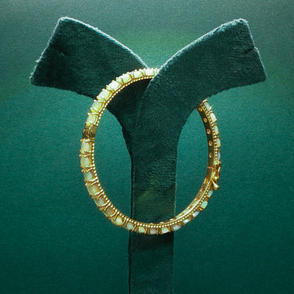 Gold hoop earring on a green stand against a green background


