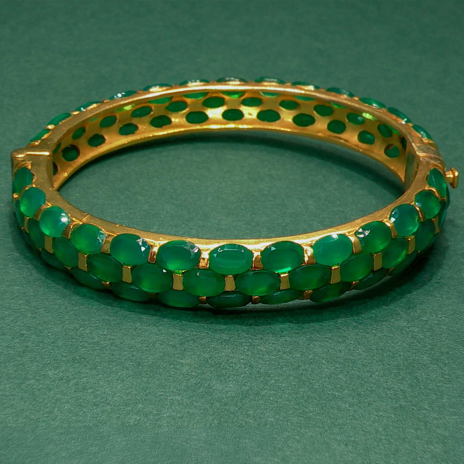Gold bracelet with green stones on a green background

