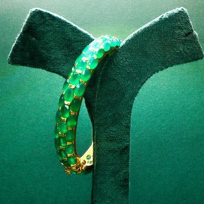 Green gemstone ring with gold setting on a green stand

