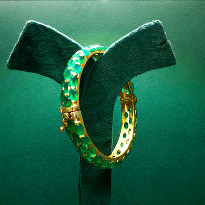 Gold hoop earrings with green gemstones on a green stand