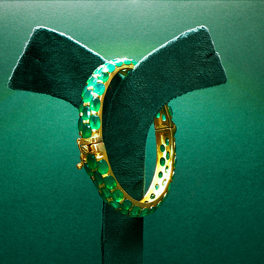 Gold hoop earrings with green gemstones on a green stand