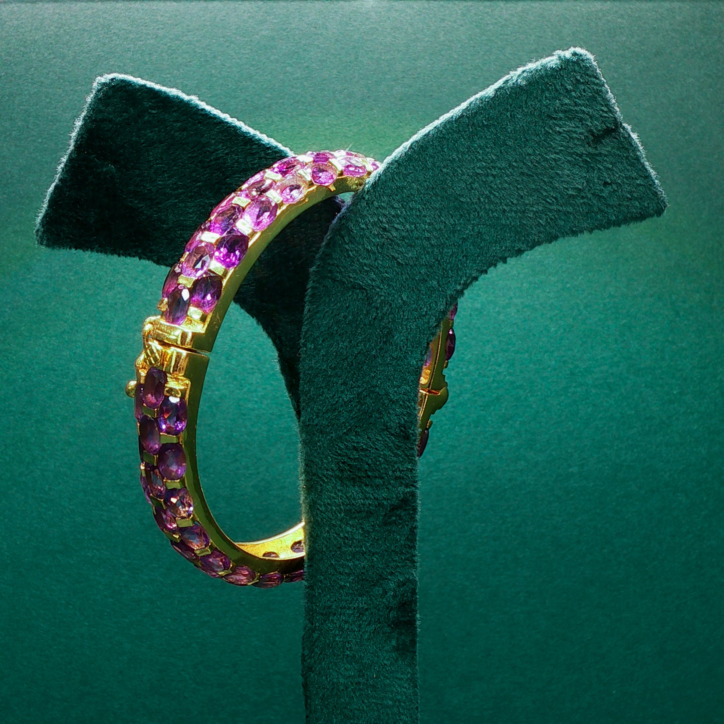 Gold hoop earrings with pink and purple gemstones on a green stand.

