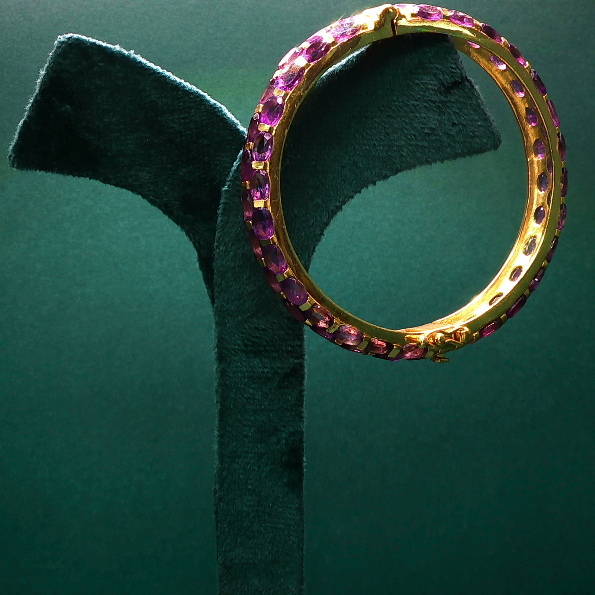 Gold ring with pink gemstones on a green stand against a green background

