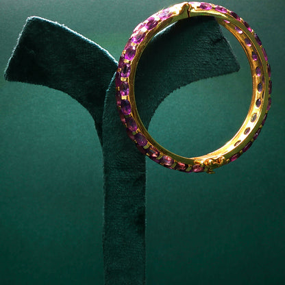 Gold ring with pink gemstones on a green stand against a green background

