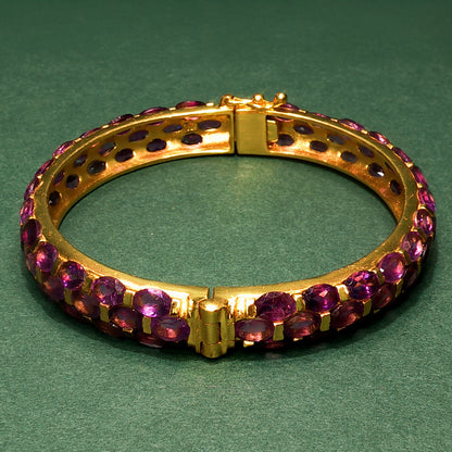 Gold bracelet with purple gemstones on a green background

