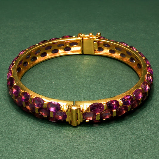 Gold bracelet with purple gemstones on a green background

