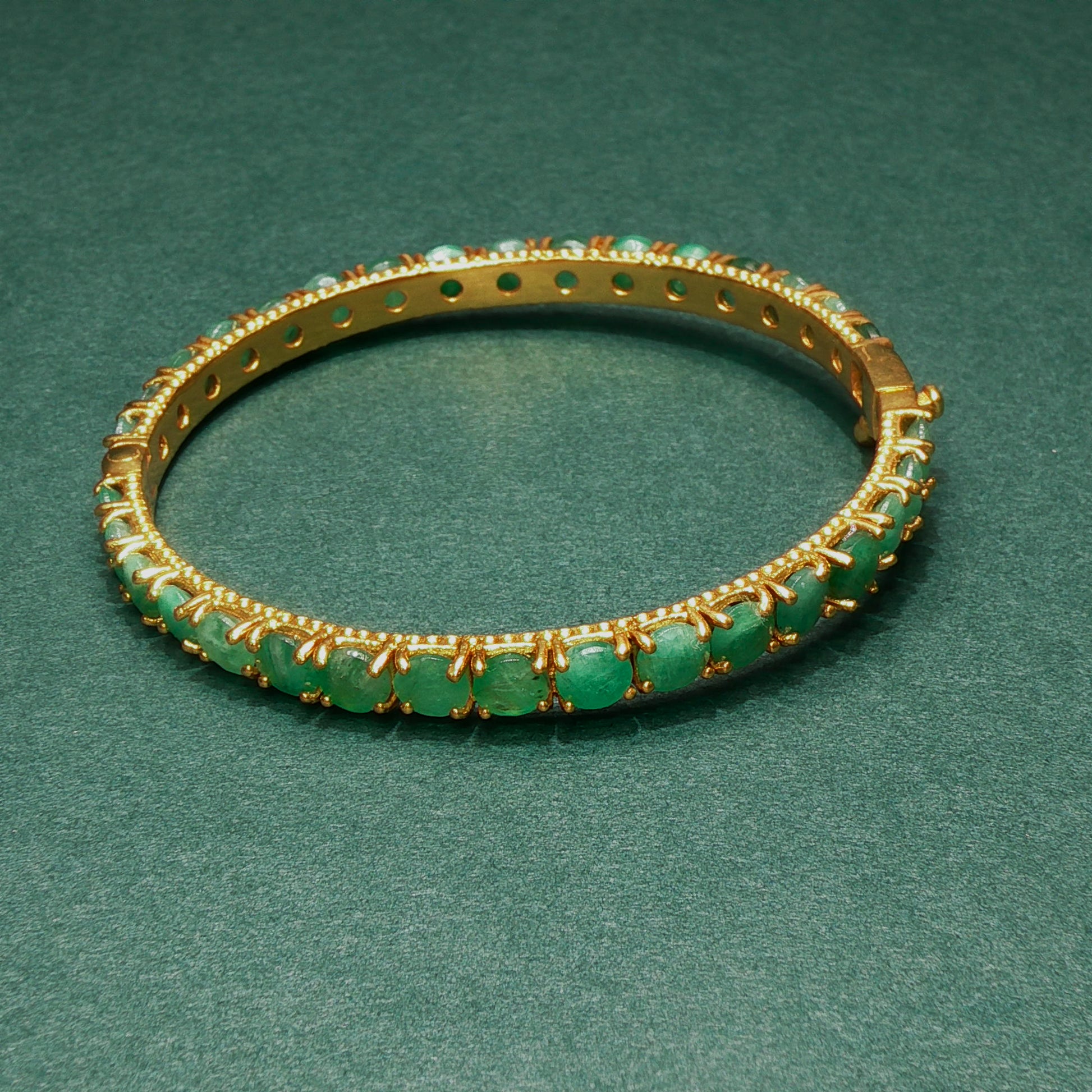 silver bracelet with green gemstones on a green background

