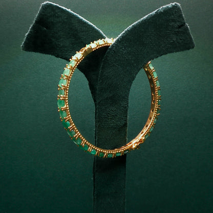 silver hoop earring with green gemstones on a green stand against a dark green background

