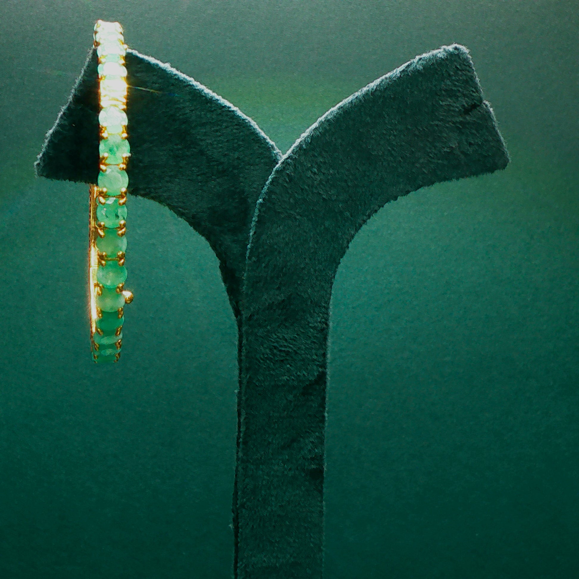 silver emerald bracelet on a green stand against a green background

