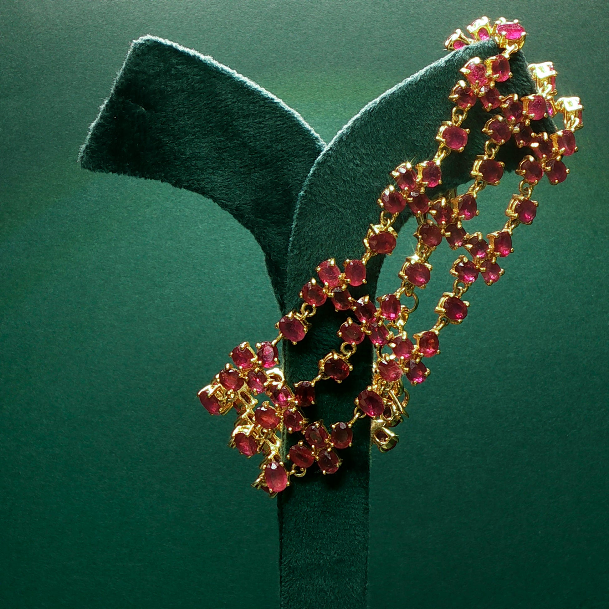 Gold necklace with red gemstones on a green stand against a green background

