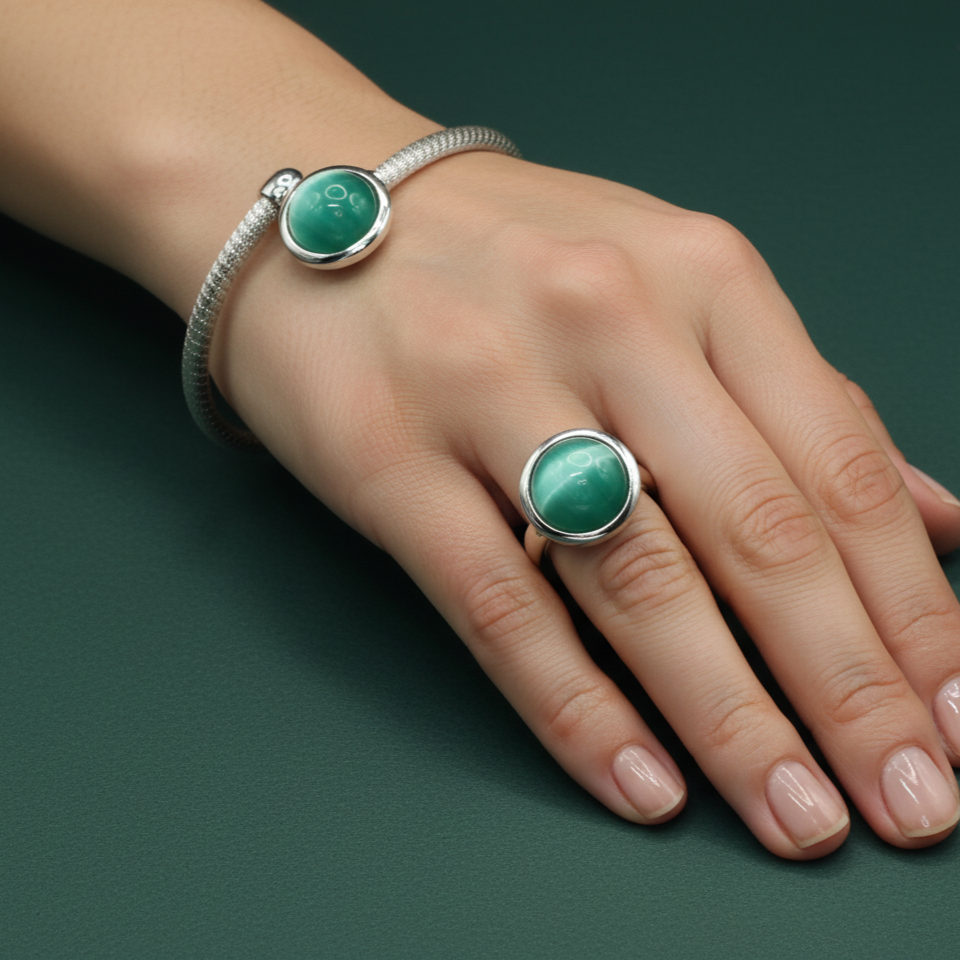 Hand wearing a silver bracelet and ring with green gemstones on a dark green background